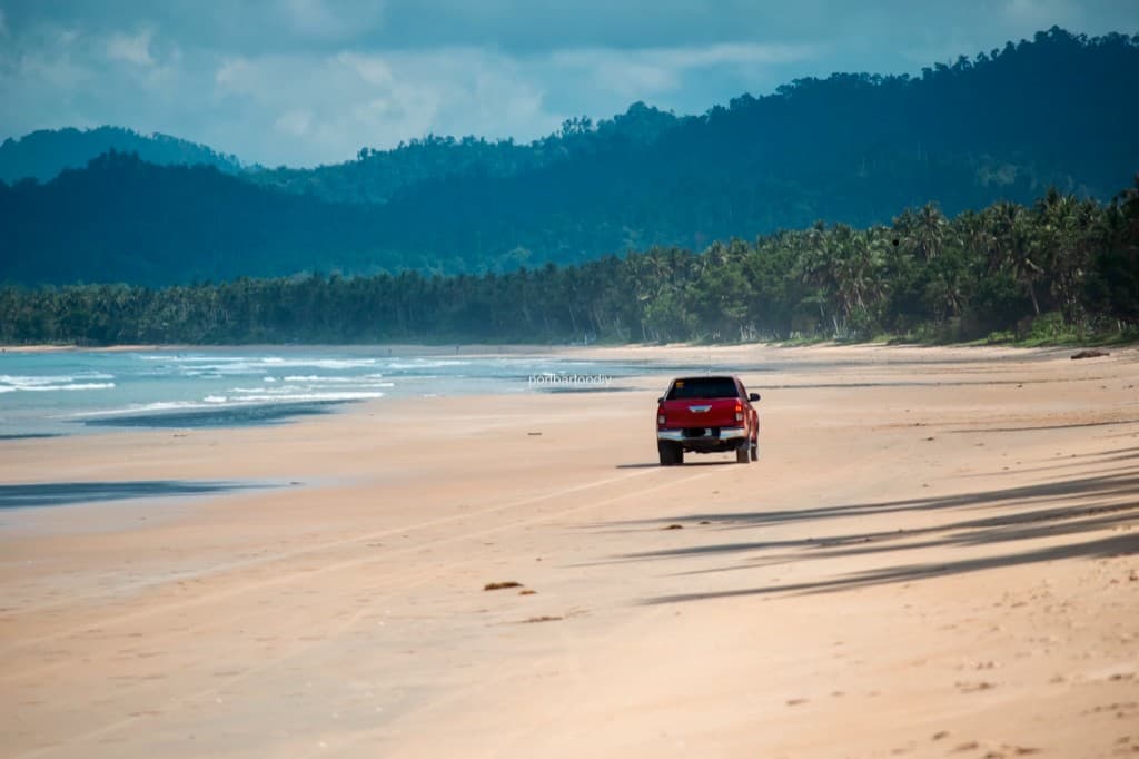 Red pickup truck driving along a wide tropical beach